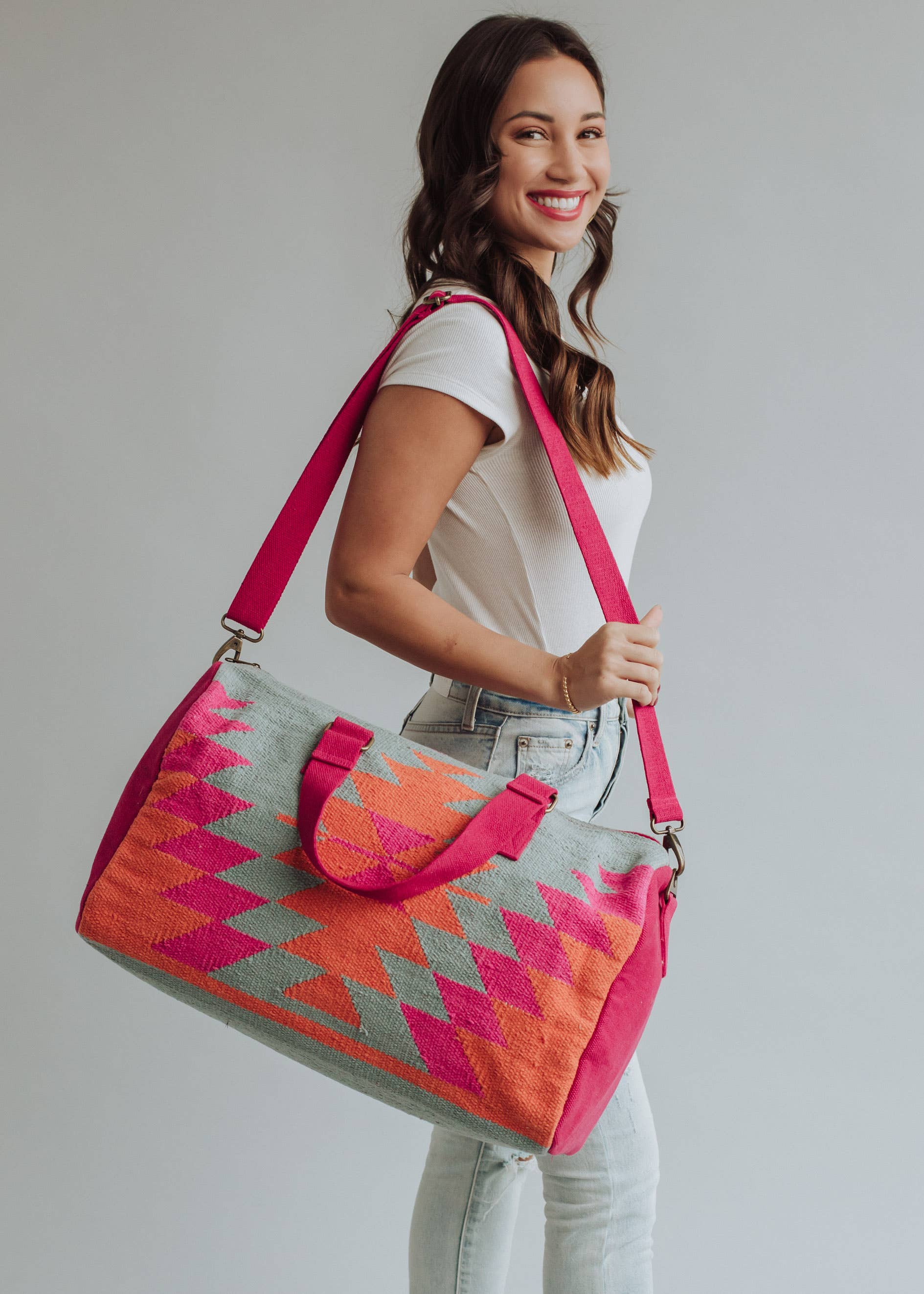 Vibrant weekender bag with orange and hot pink geometric design, held by woman in light wash jeans and white tank top