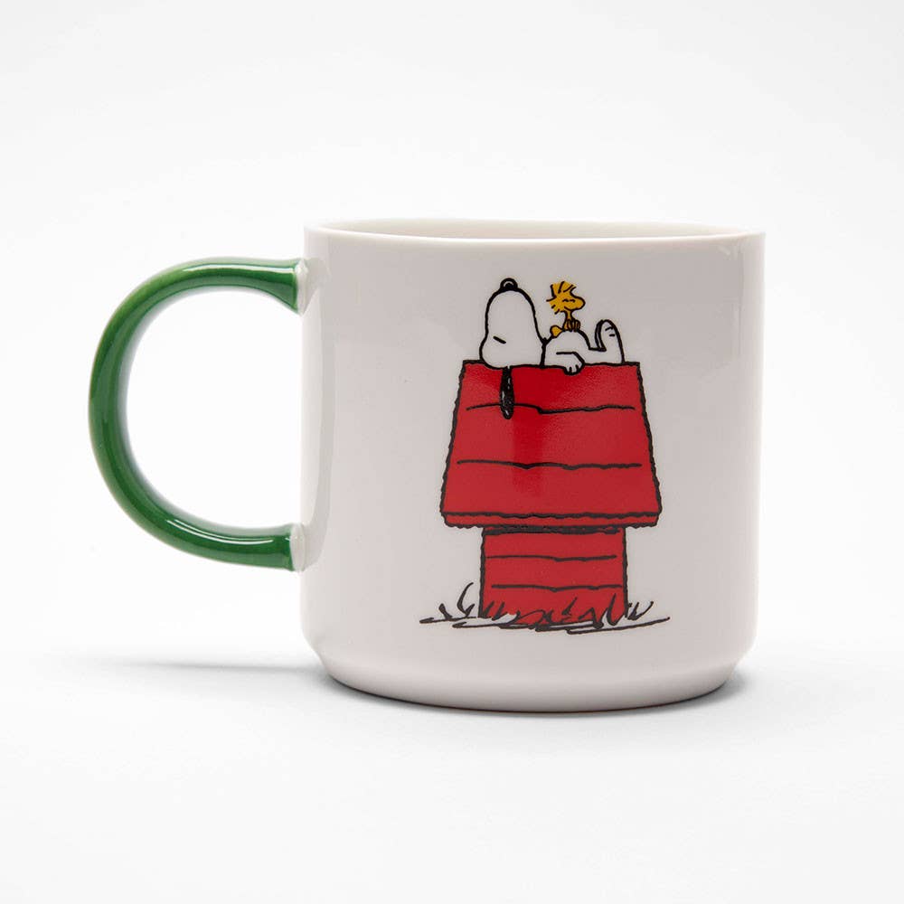 White ceramic mug with a green handle, featuring a beagle and a bird on a red doghouse, along with a group of characters enjoying music.