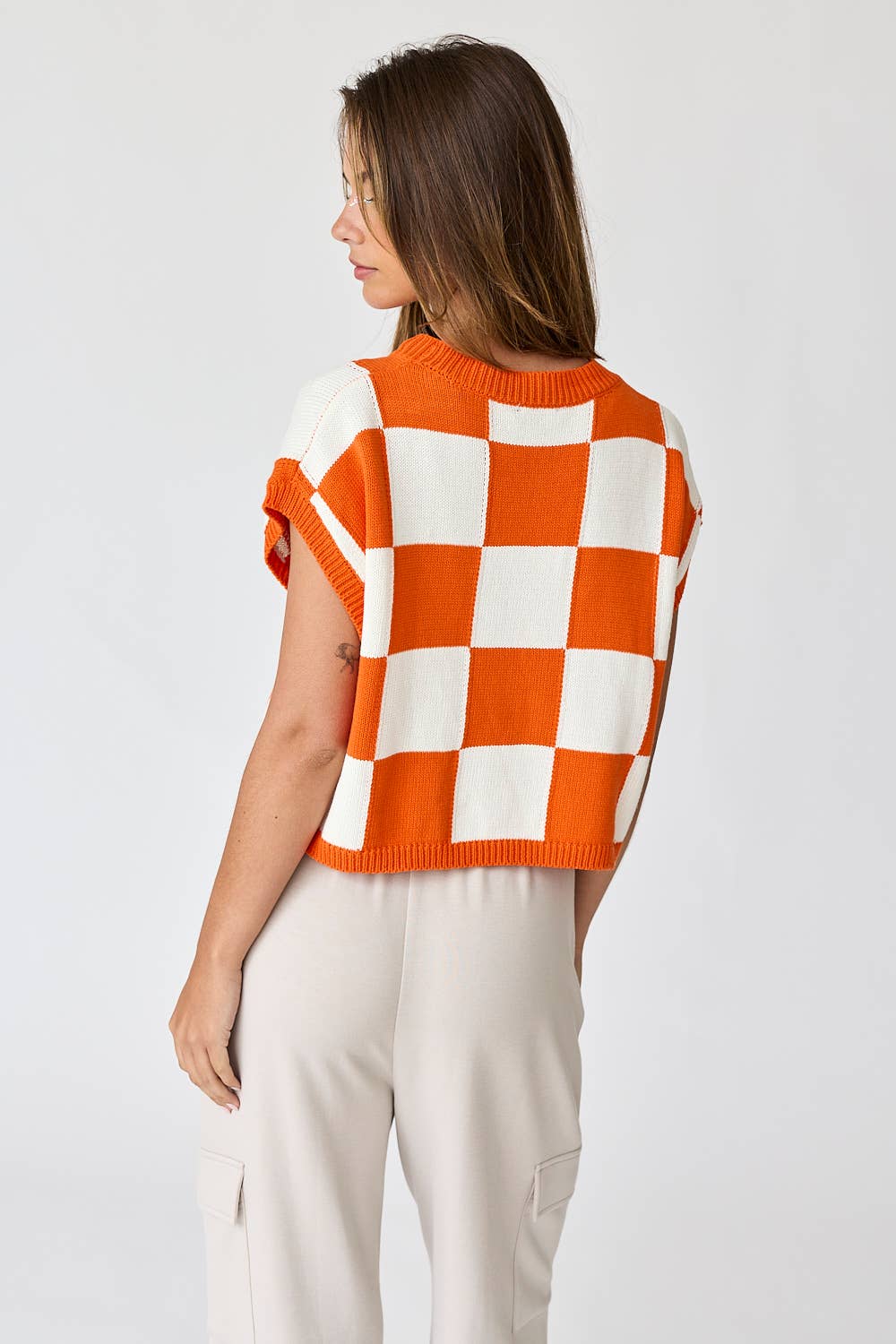 Woman wearing an orange and white loose-fit checker knit top with beige pants.
