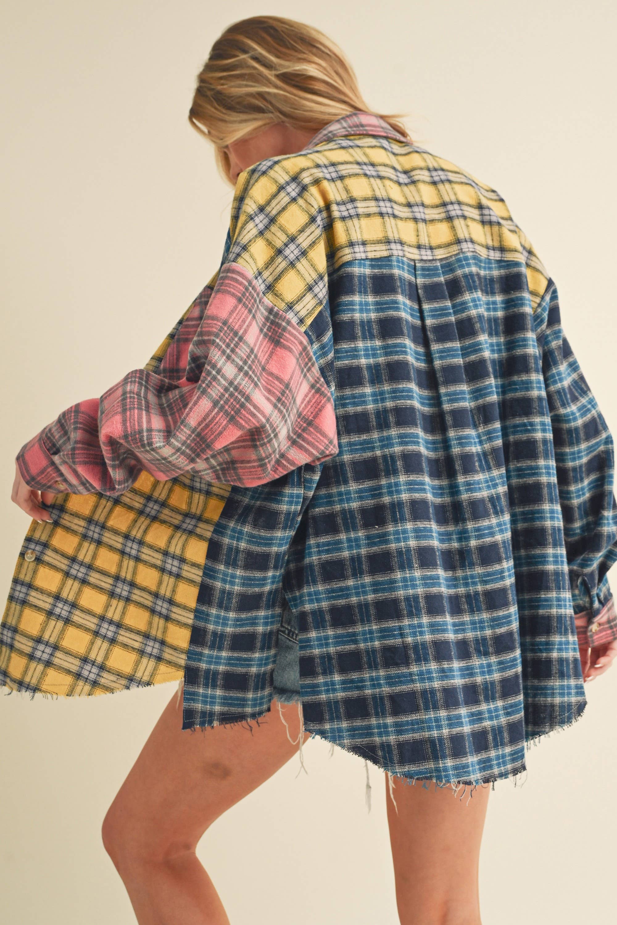 Woman wearing an oversized plaid colorblock flannel shirt in pink, yellow, and navy tones with raw hems.