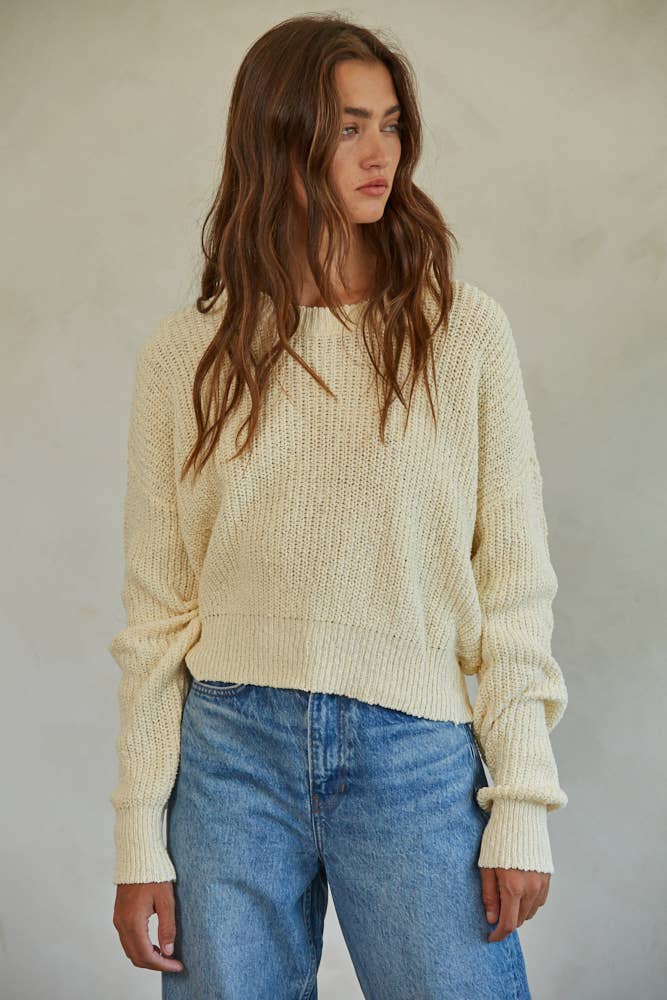 Woman wearing a cream chunky knit pullover sweater with relaxed fit, styled casually with light-wash jeans.