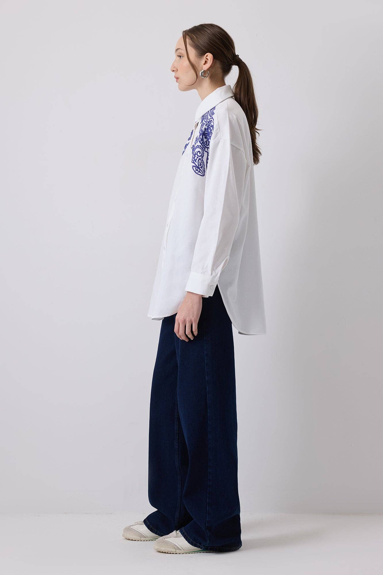 Woman wearing a white oversized shirt with bold blue embroidery on shoulders