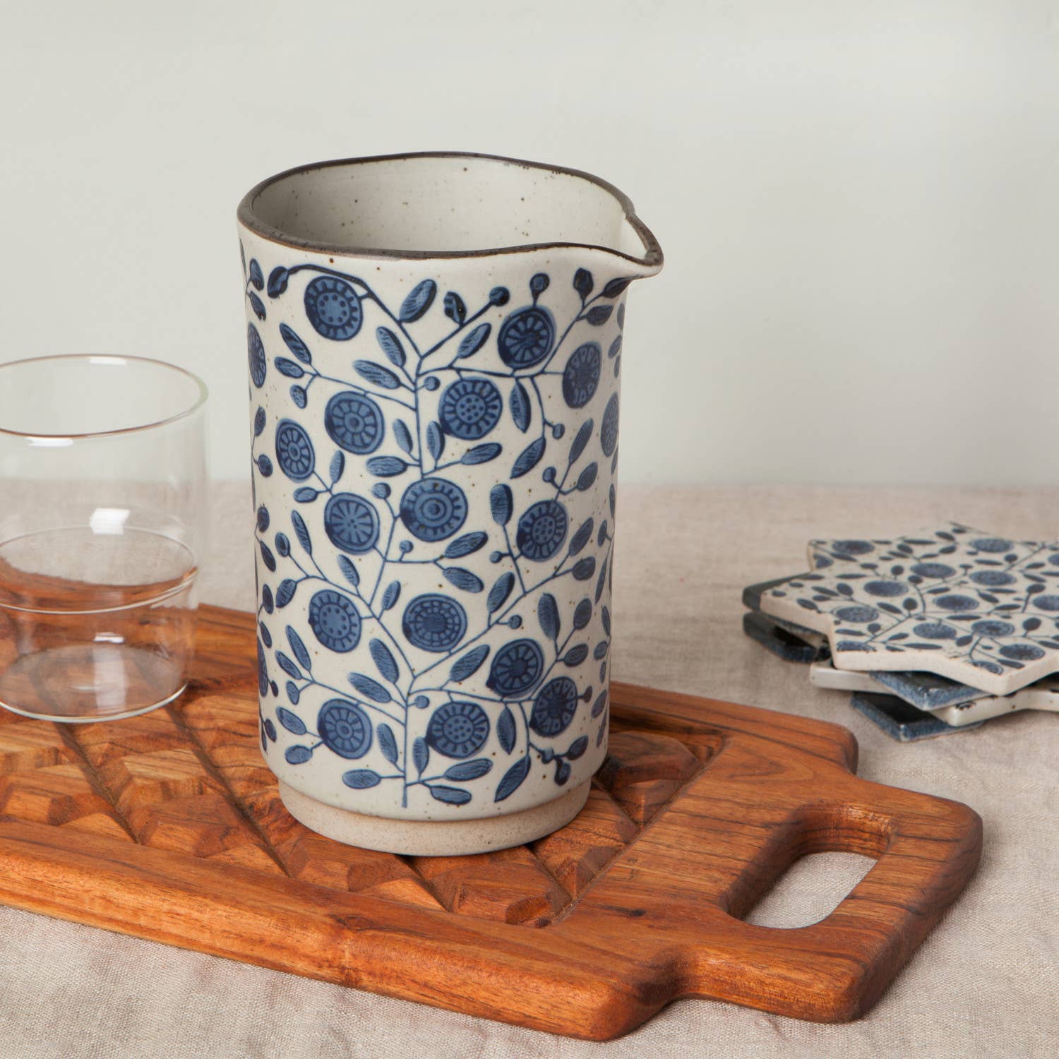 Handmade ceramic pitcher with speckled glaze and blue floral pattern, featuring a curved spout for easy pouring.