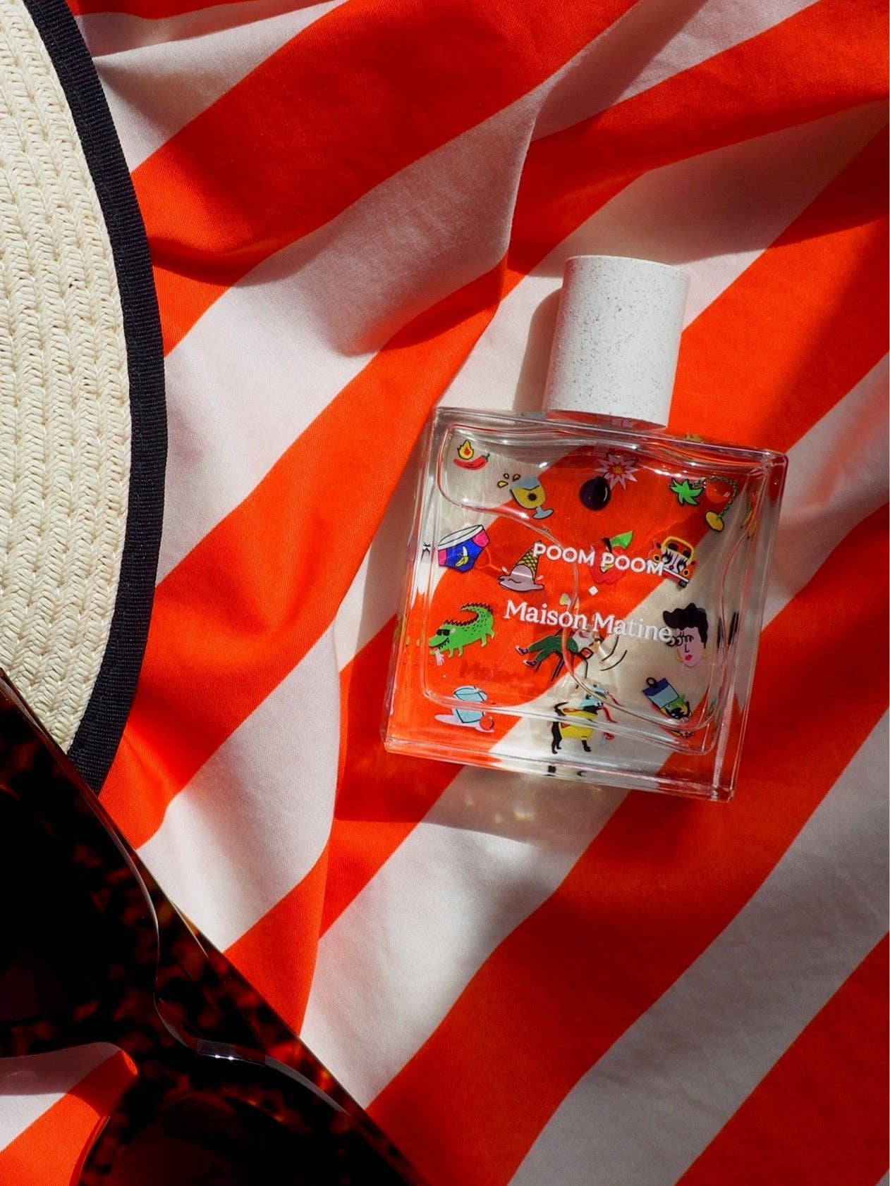 Poom Poom Eau de Parfum bottle with playful illustrations, displayed on an orange and white striped fabric background.