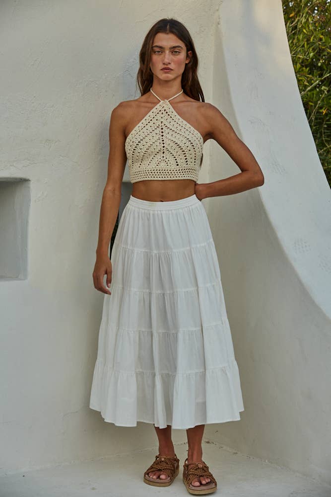 Model wearing a crochet halter crop top in black and cream, styled with jeans and a skirt, showing detailed open-stitch design.