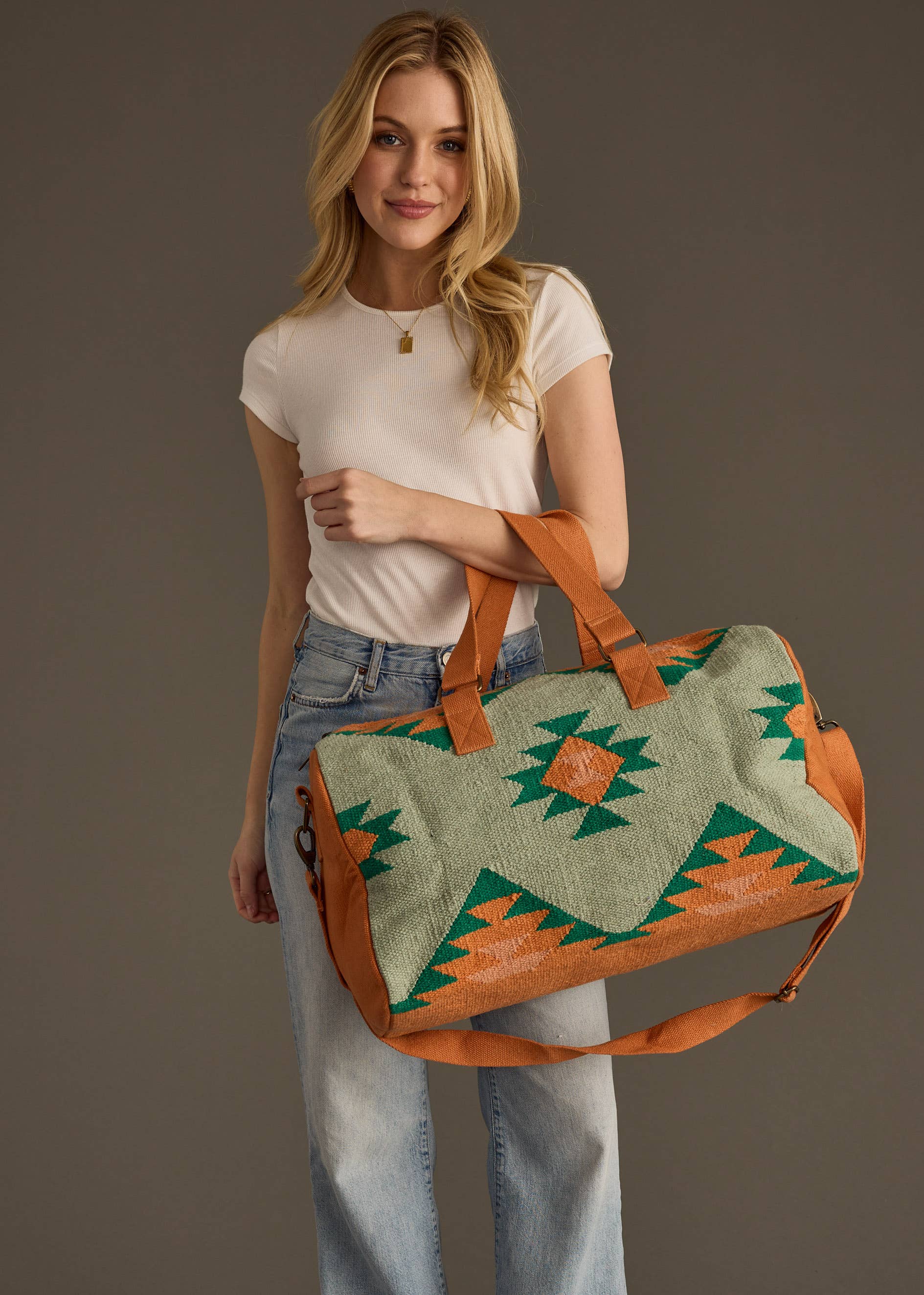Sage green and rust weekender bag with geometric tribal pattern in green and orange, held by woman in jeans and white tank