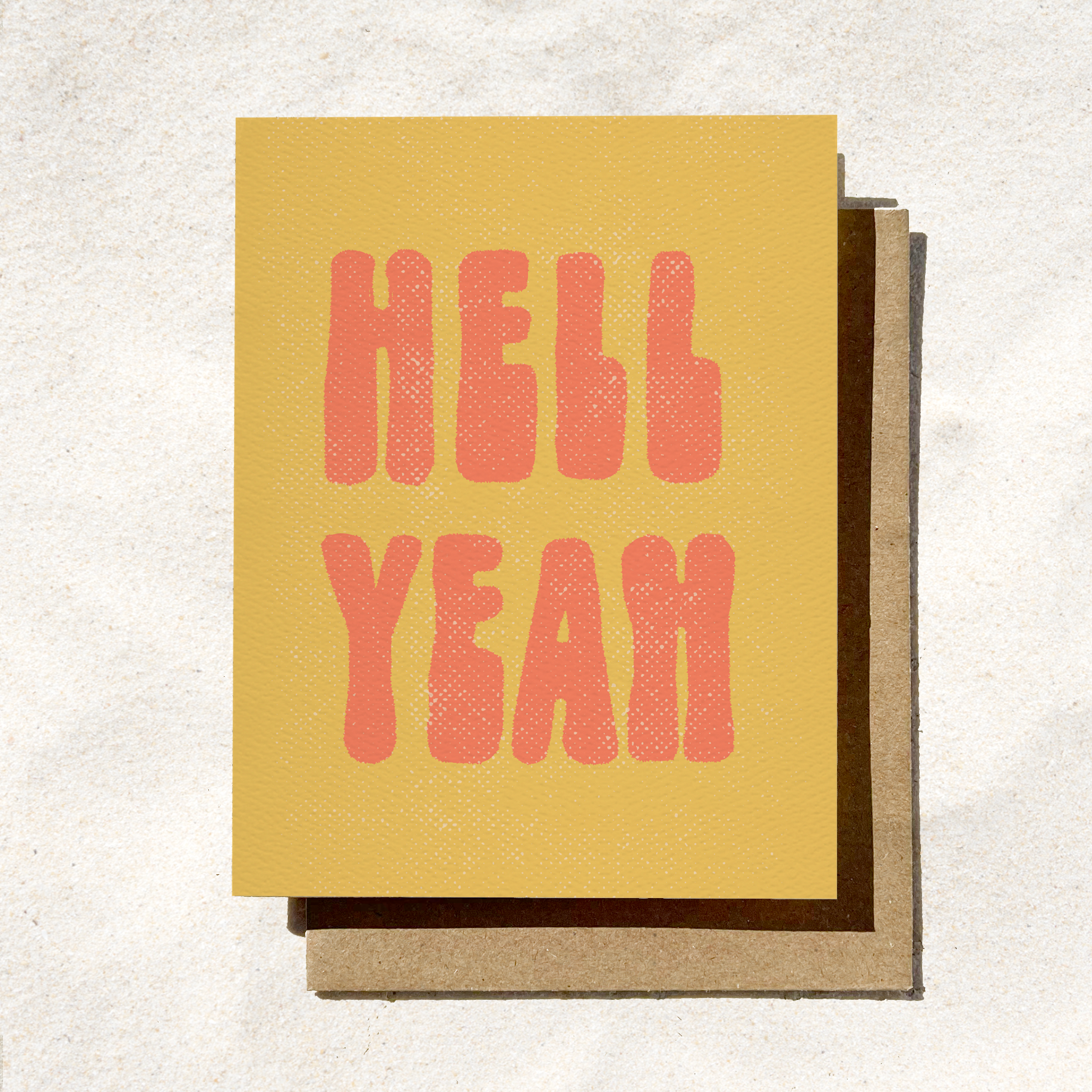 A yellow greeting card with the text 'HELL YEAH' in red, bold, retro-style lettering, accompanied by a brown envelope.