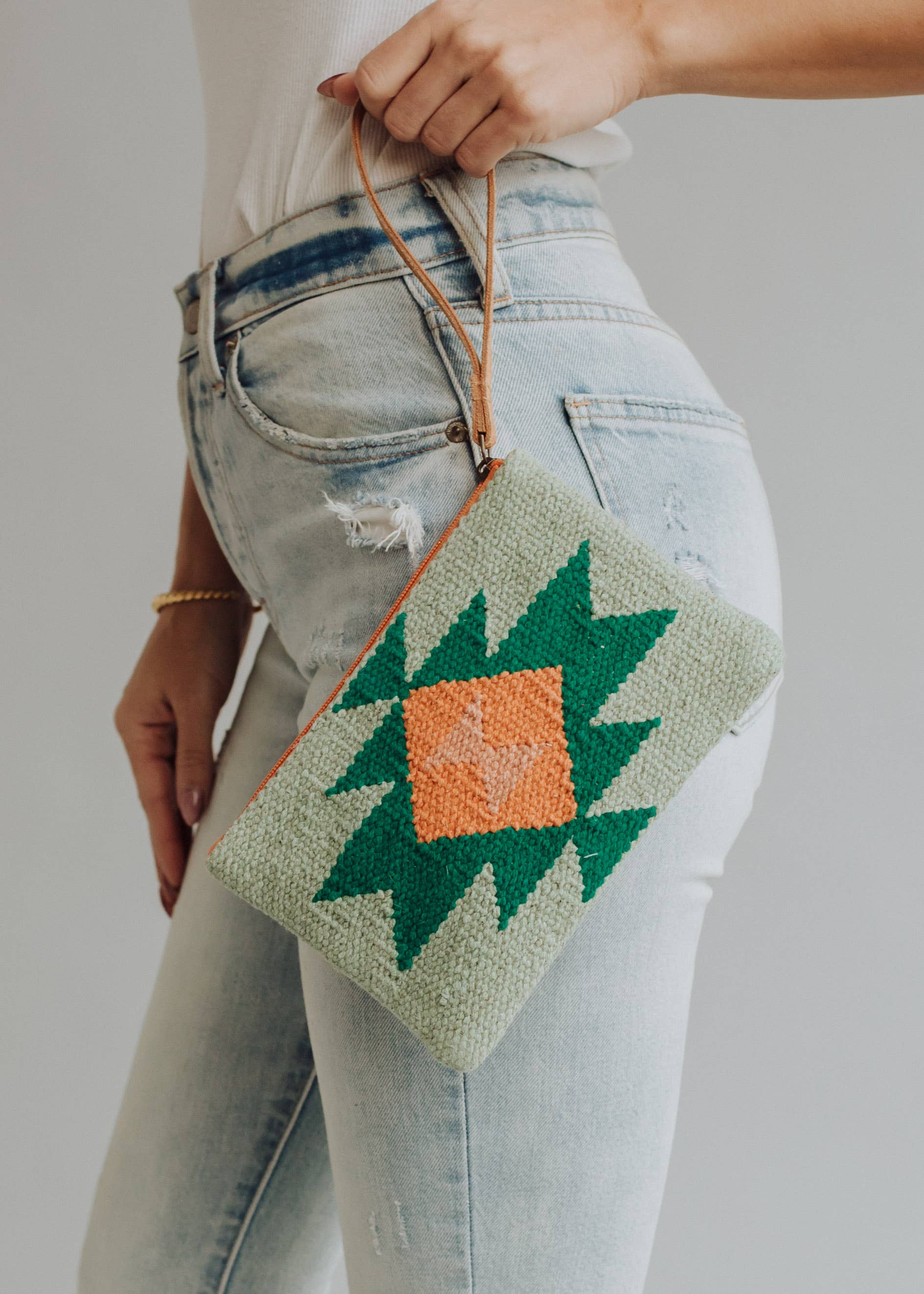 Sage green woven wristlet with orange and emerald geometric pattern, worn with light denim