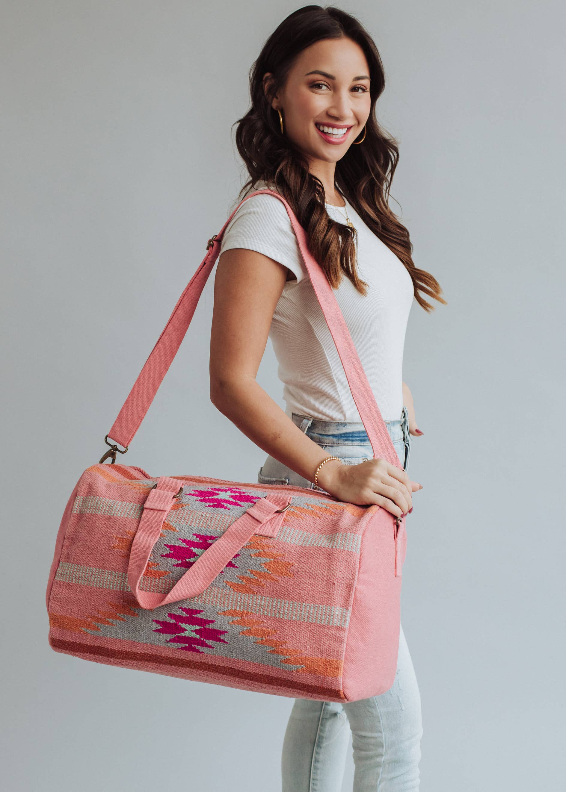 Woman holding a pink and orange woven weekender duffel bag with fuchsia geometric design