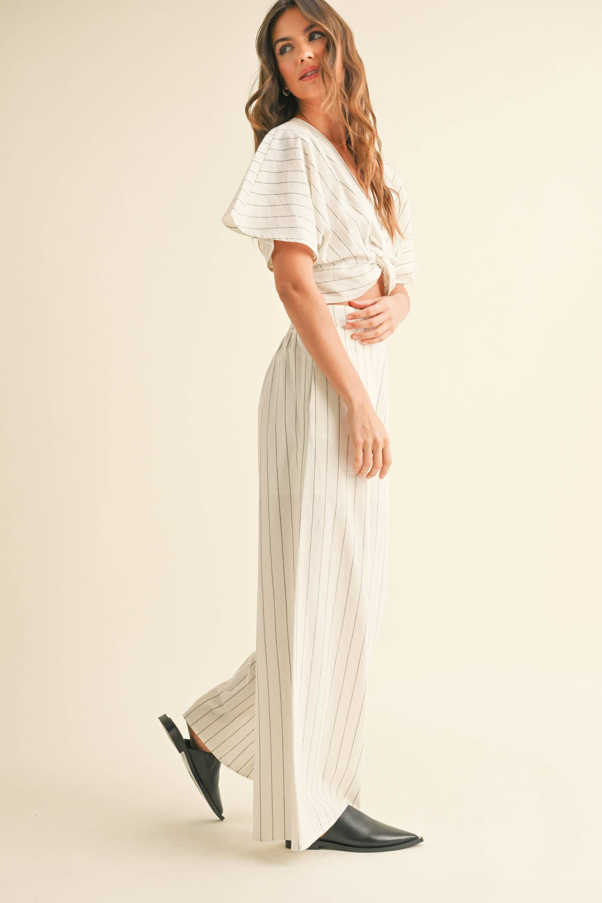 Woman wearing a two-piece striped set with a twist-front crop top and wide-leg pants in cream and tan color options.