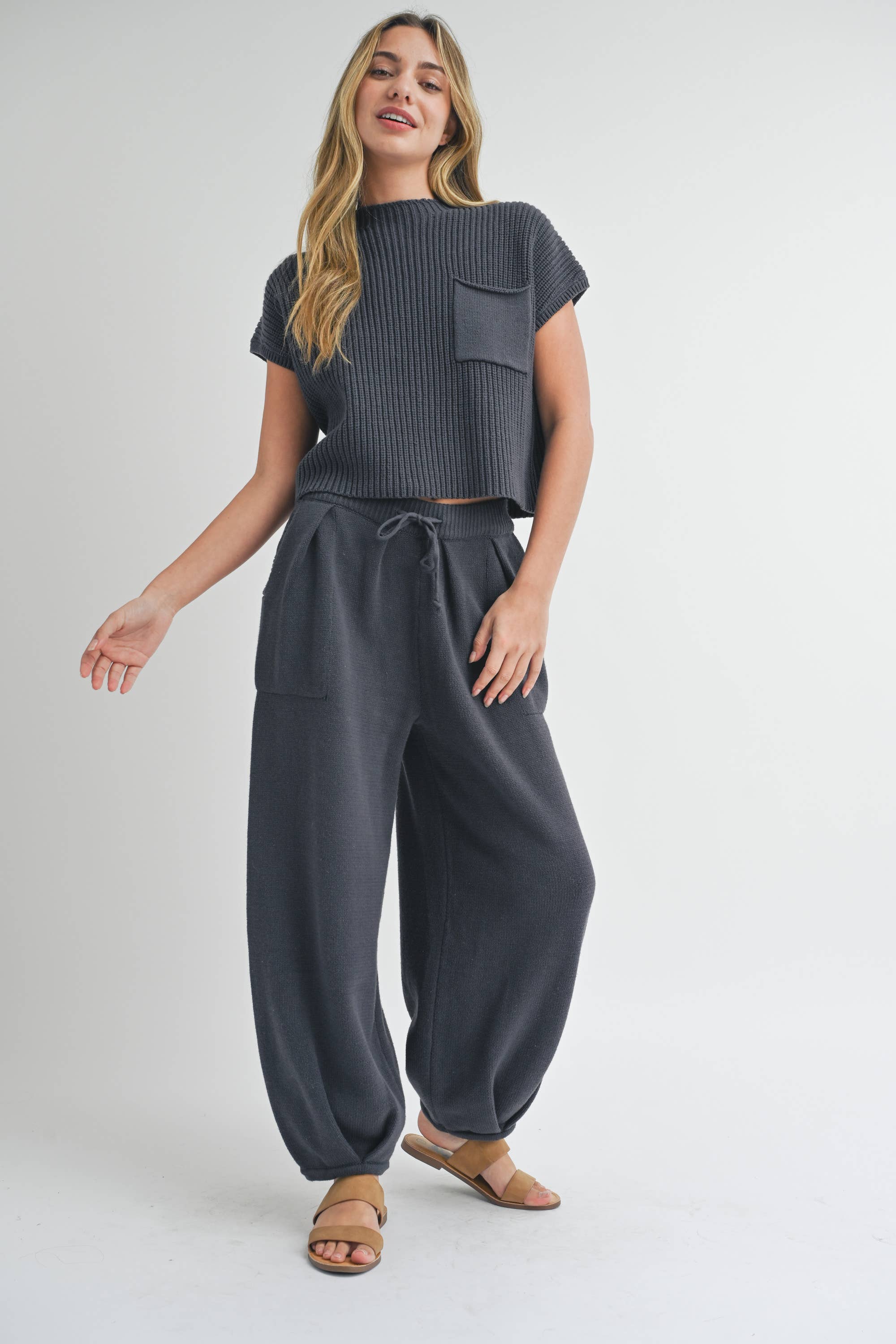 Woman wearing pleated bottom knitted pants in relaxed fit with drawstring waist and ankle detail.
