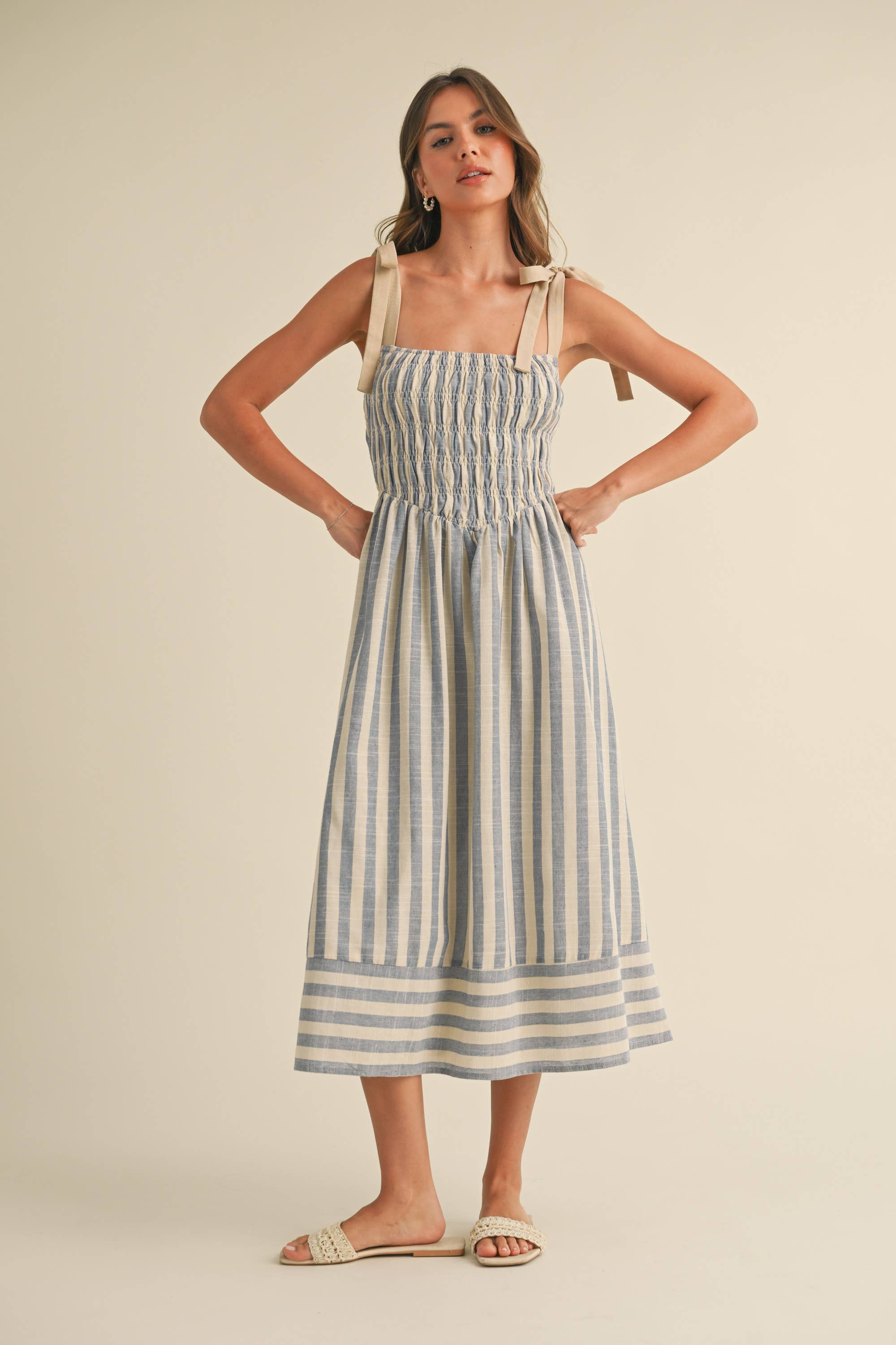 Woman wearing a blue and cream striped midi dress with smocked bodice and tie shoulder straps.
