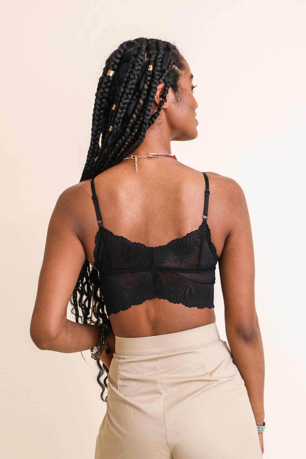 Model wearing a scalloped-edge lace bralette in burgundy and blue tones, styled with layered necklaces and velvet pants.
