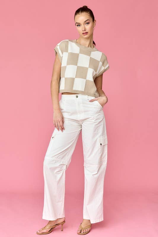 Woman wearing a taupe and white loose-fit checker knit top with white pants.