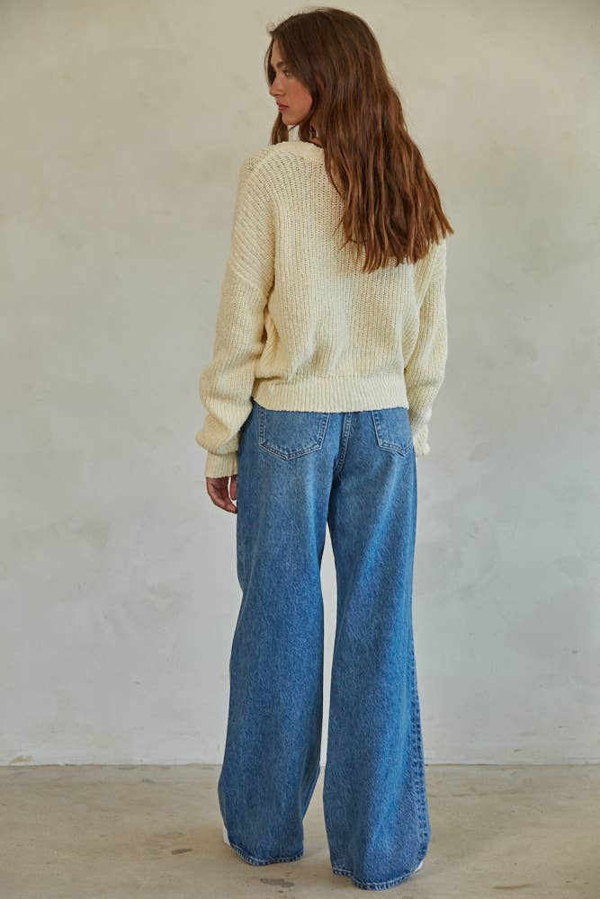 Woman wearing a cream chunky knit pullover sweater with relaxed fit, styled casually with light-wash jeans.