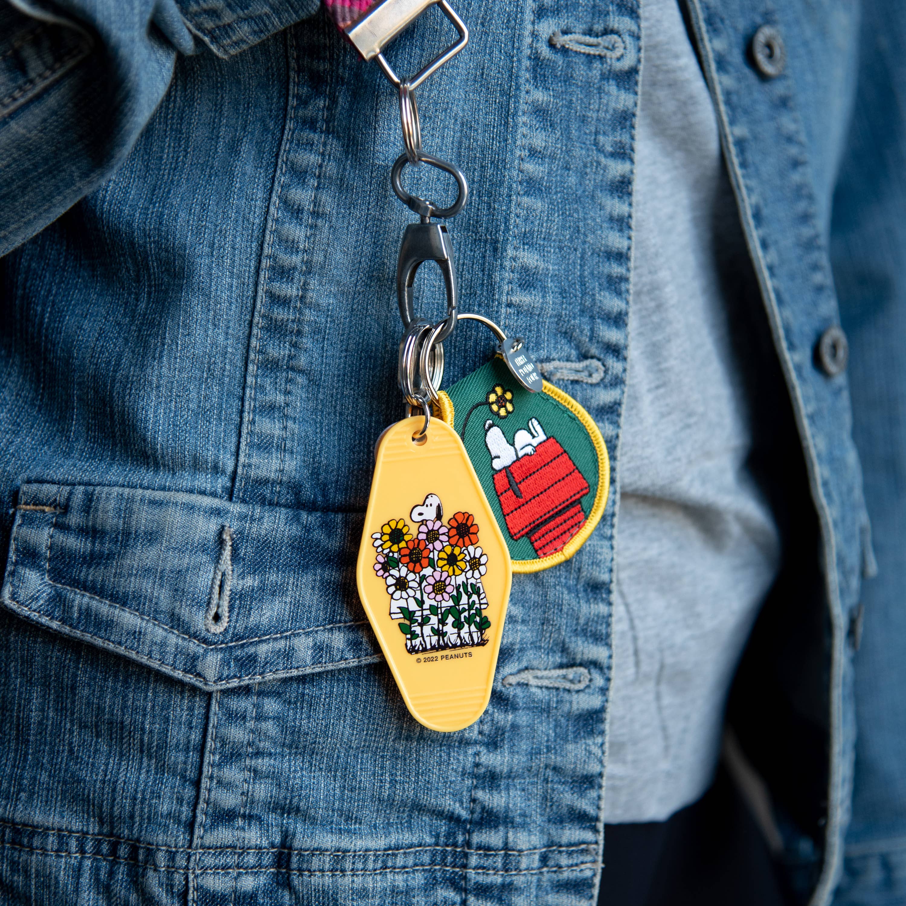 Peanuts® Snoopy Daisy Garden Key Tag featuring Snoopy surrounded by colorful daisies on a vibrant yellow background.