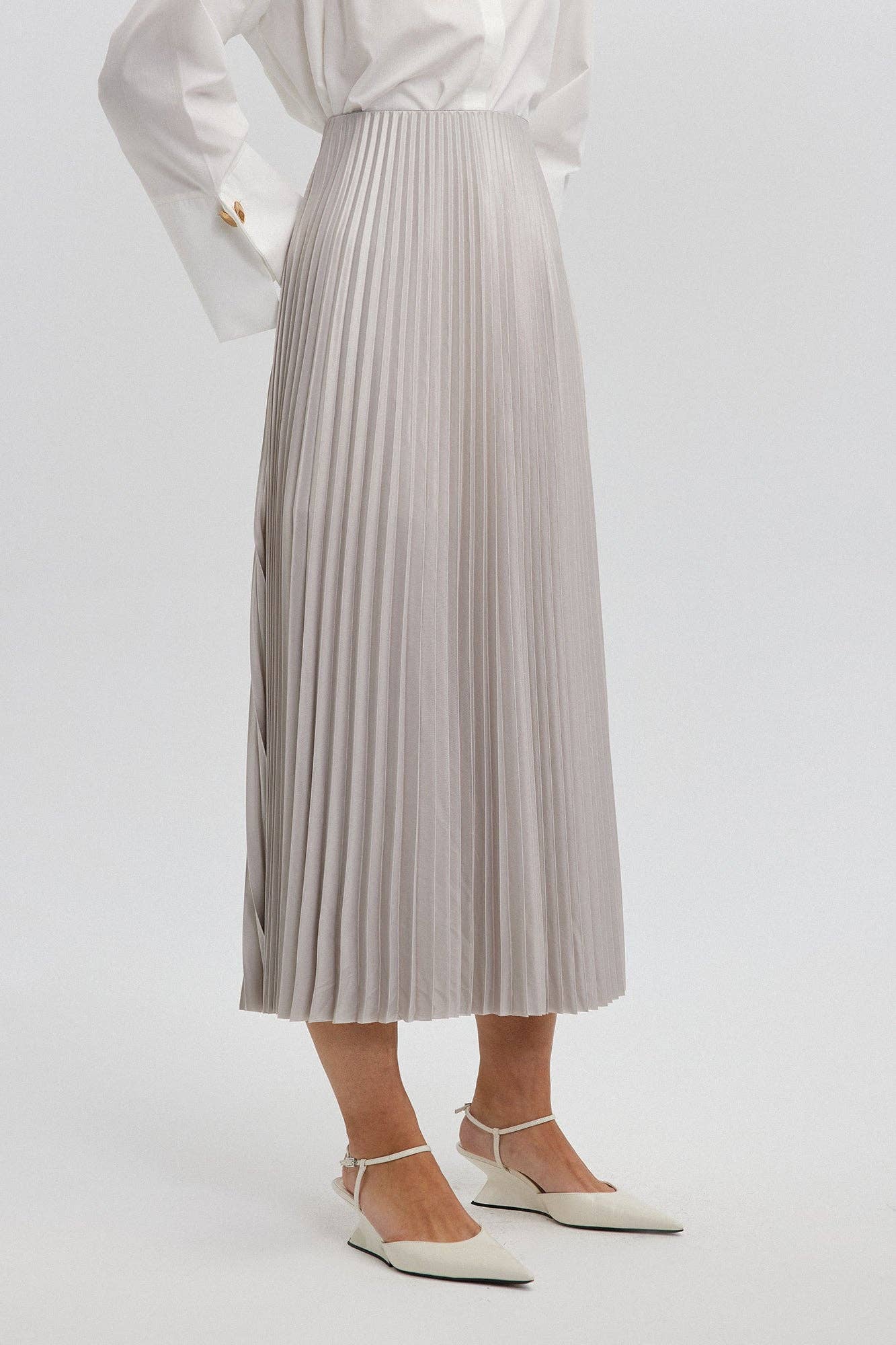 Model wearing a high-waisted pleated maxi skirt styled with a white blouse and pointed heels.