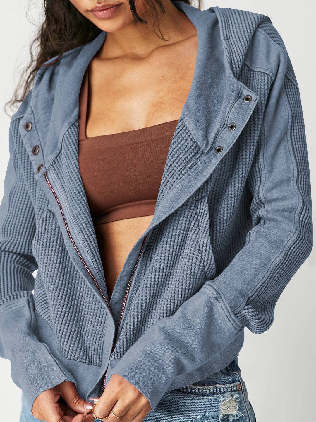 Woman wearing a Sahara Sky Hooded Jacket with a zip-up front, textured waffle knit, and button detailing in blue and brown tones.