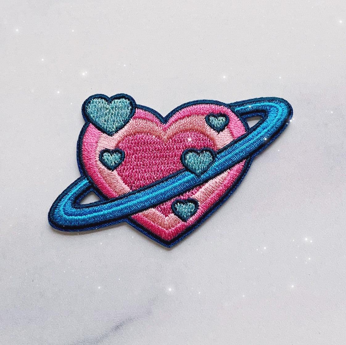 Embroidered patch showcasing a planet in the form of a heart with intricate details.