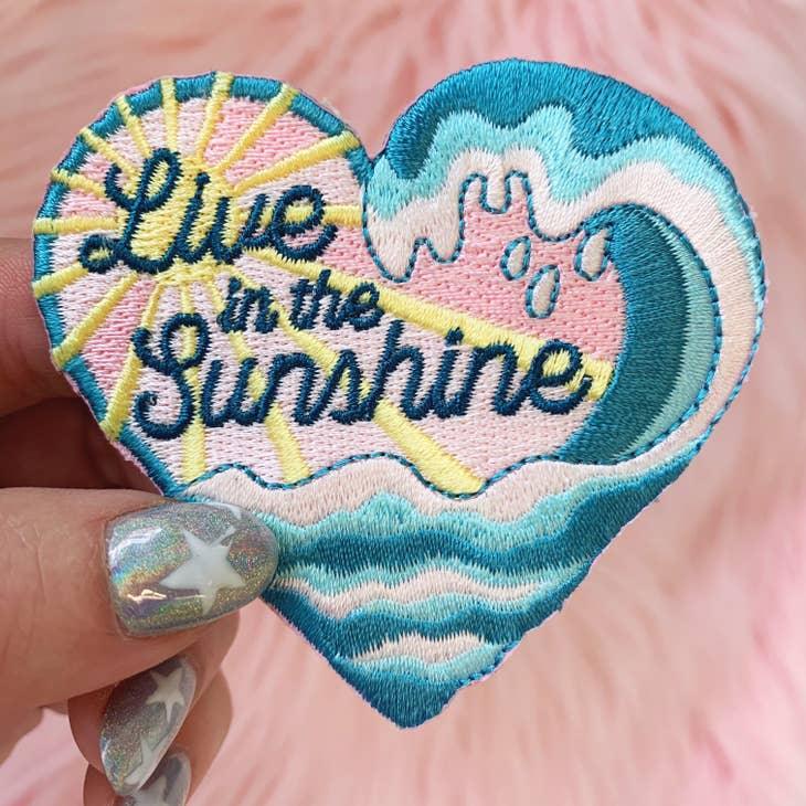 Brightly colored embroidered patch with the words "Live in The Sunshine" surrounded by radiant sun rays.
