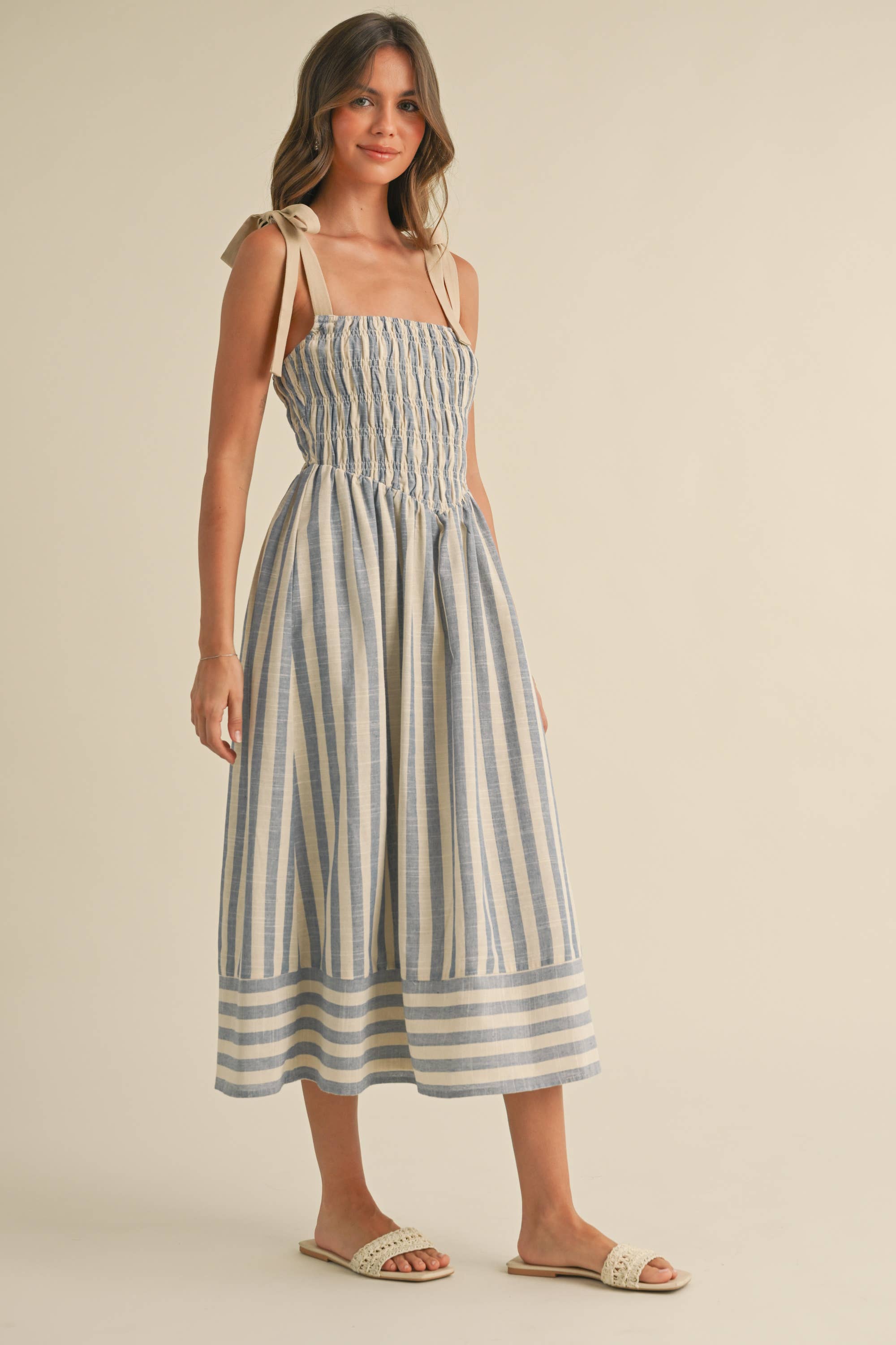 Woman wearing a blue and cream striped midi dress with smocked bodice and tie shoulder straps.