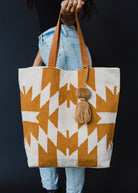 Large mustard and ivory woven tote bag with geometric pattern, leather handles, and a tassel accent