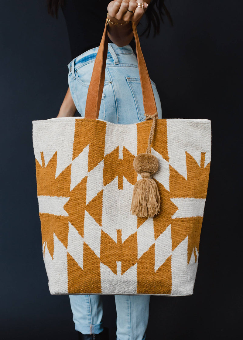 Large mustard and ivory woven tote bag with geometric pattern, leather handles, and a tassel accent