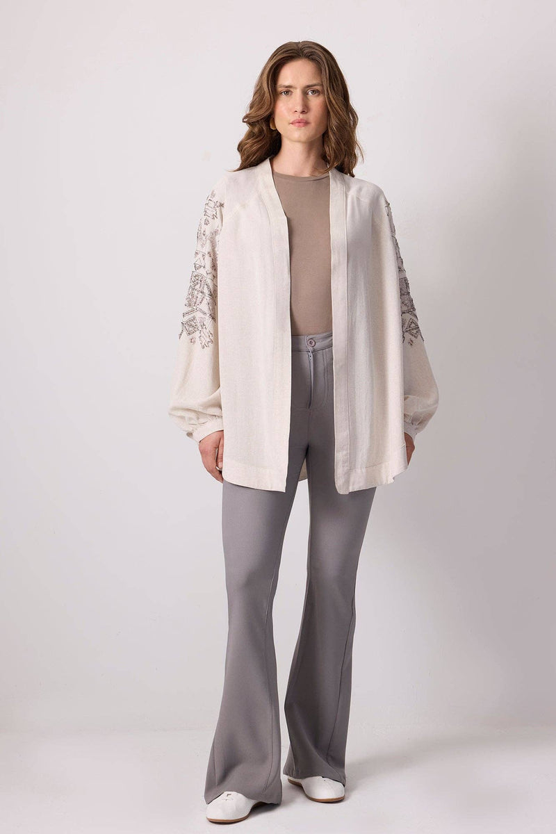 Woman wearing a cream linen kimono jacket with silver sequin embroidery on the sleeves and back.