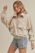 Woman wearing an oversized teal fleece pullover with a quarter zip and black leggings; Woman in a beige fleece pullover with a quarter zip and denim shorts.