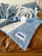 Soft chambray blue plush throw with palm tree design, perfect for cozying up or adding a beachy touch to any space.