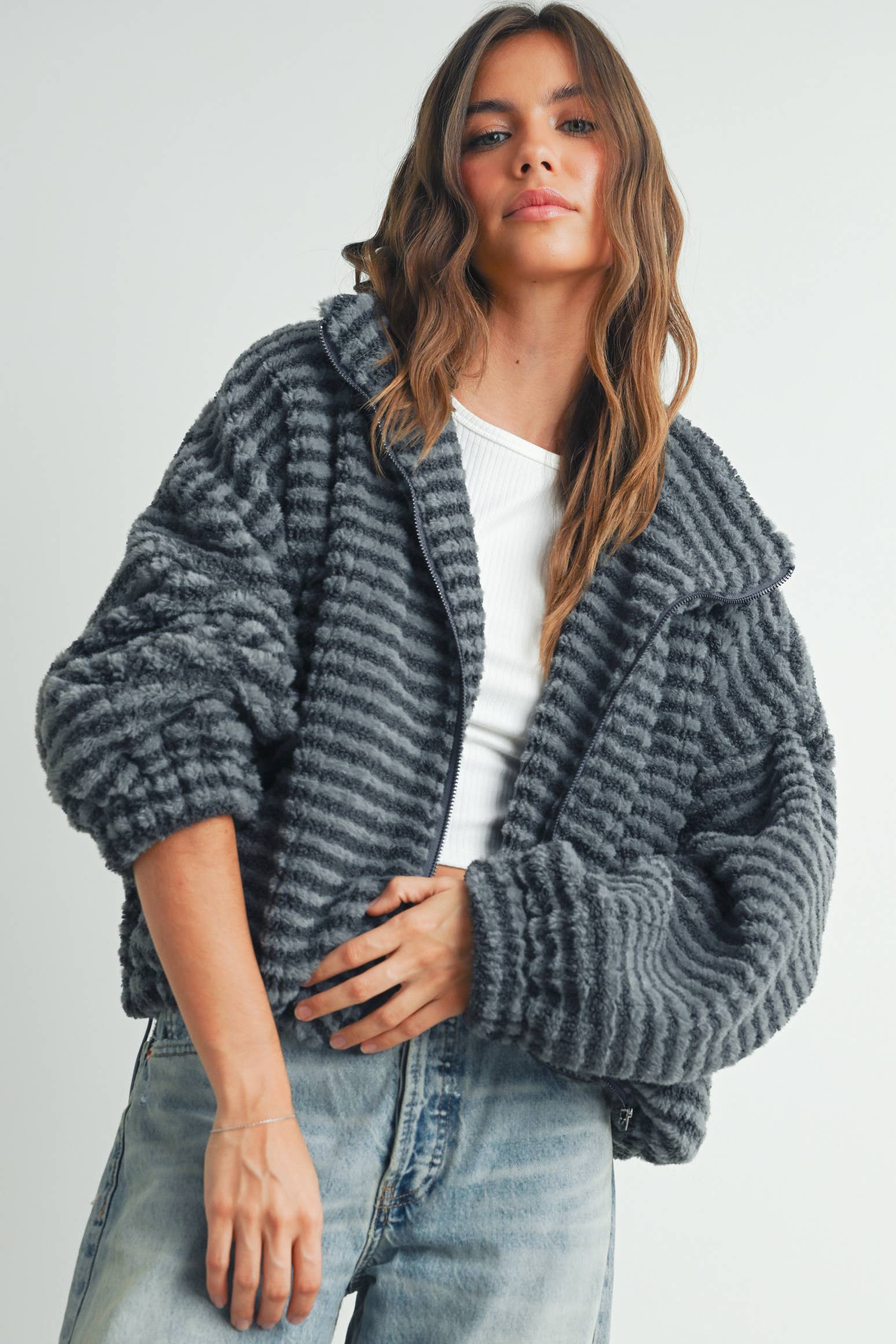 Woman wearing a ribbed gray faux-fur jacket paired with a white tank top and jeans.
