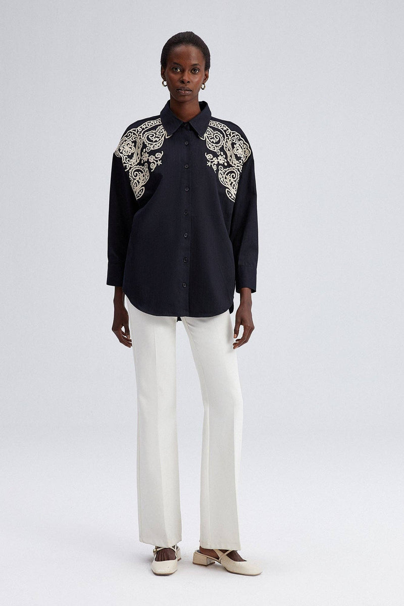 Model wearing black oversized shirt with cream embroidery on shoulders and front yoke.