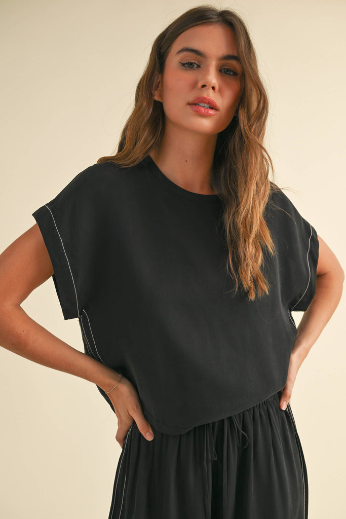 Model wearing a black two-piece lounge set with white contrast stitching, featuring a cap-sleeve top and drawstring wide-leg pants.
