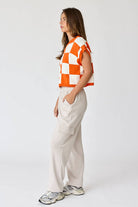 Woman wearing an orange and white loose-fit checker knit top with beige pants.