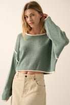Woman wearing a sage green off-shoulder cropped sweater with white trim details and long sleeves.
