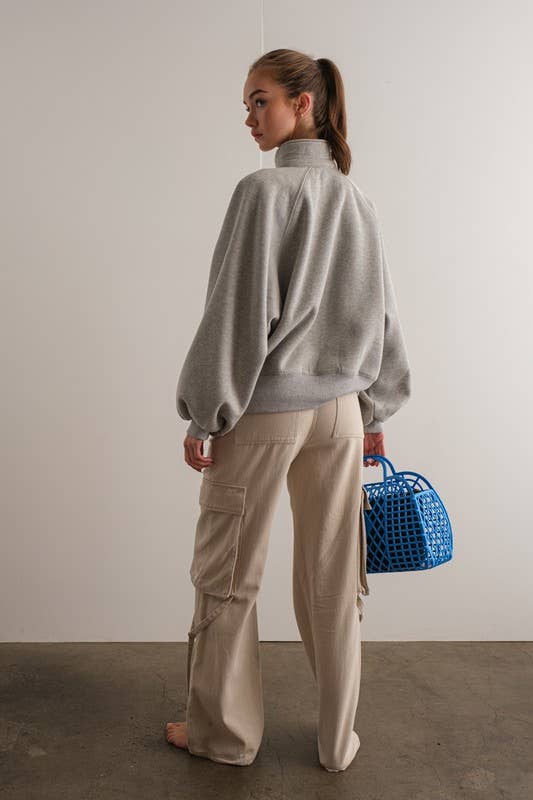 Woman wearing an oversized gray pullover sweatshirt with quarter snaps and voluminous sleeves, paired with beige pants.