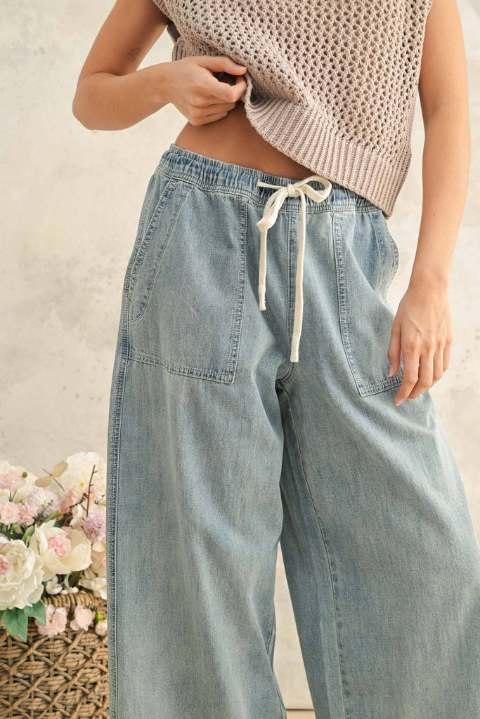 Woman wearing light wash wide-leg denim pants with elastic drawstring waist and front patch pockets.