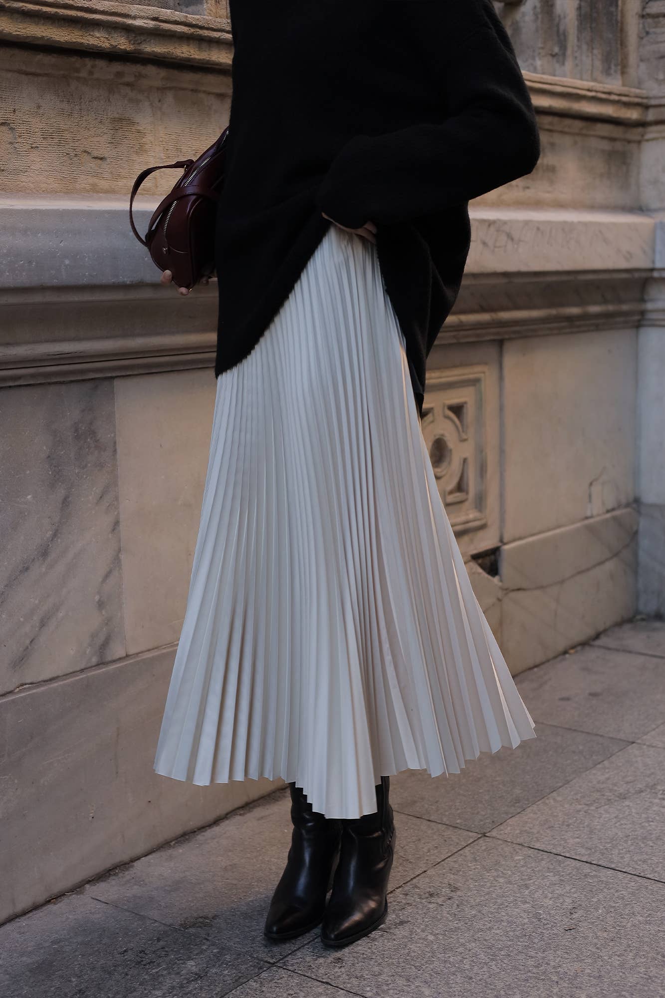 Model wearing a high-waisted pleated maxi skirt styled with a white blouse and pointed heels.