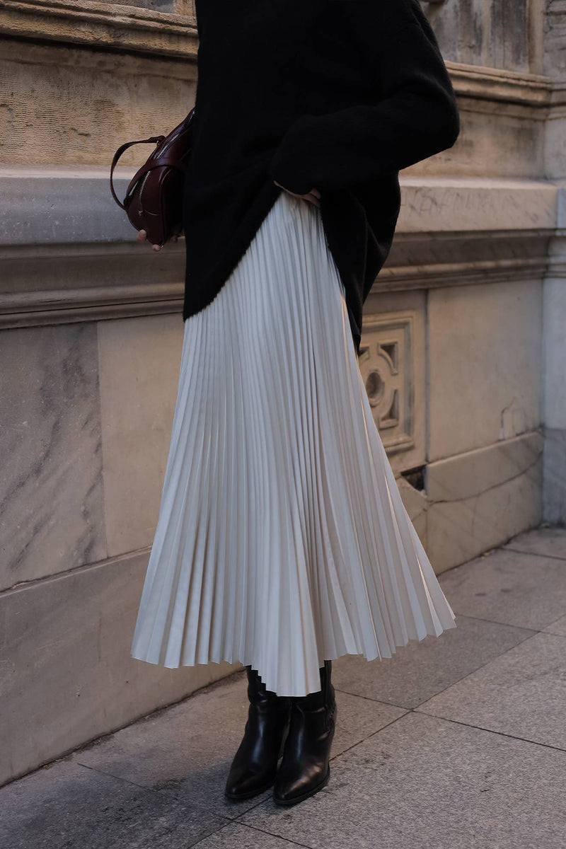 Model wearing a high-waisted pleated maxi skirt styled with a white blouse and pointed heels.