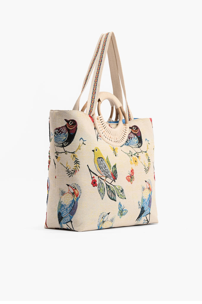 Beige embroidered tote bag with colorful birds, butterflies, and leaves, featuring round woven handles and shoulder strap.