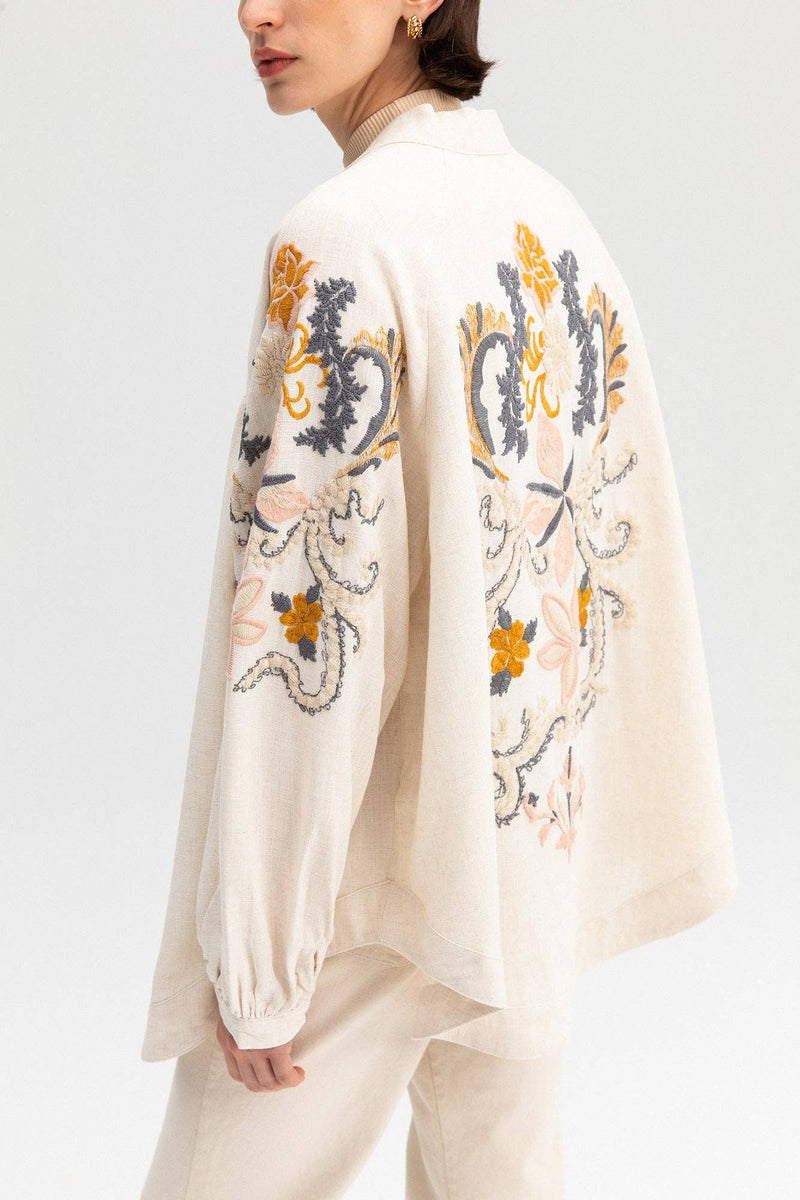 Back view of a cream-colored kimono jacket with colorful floral embroidery, worn with matching light trousers.