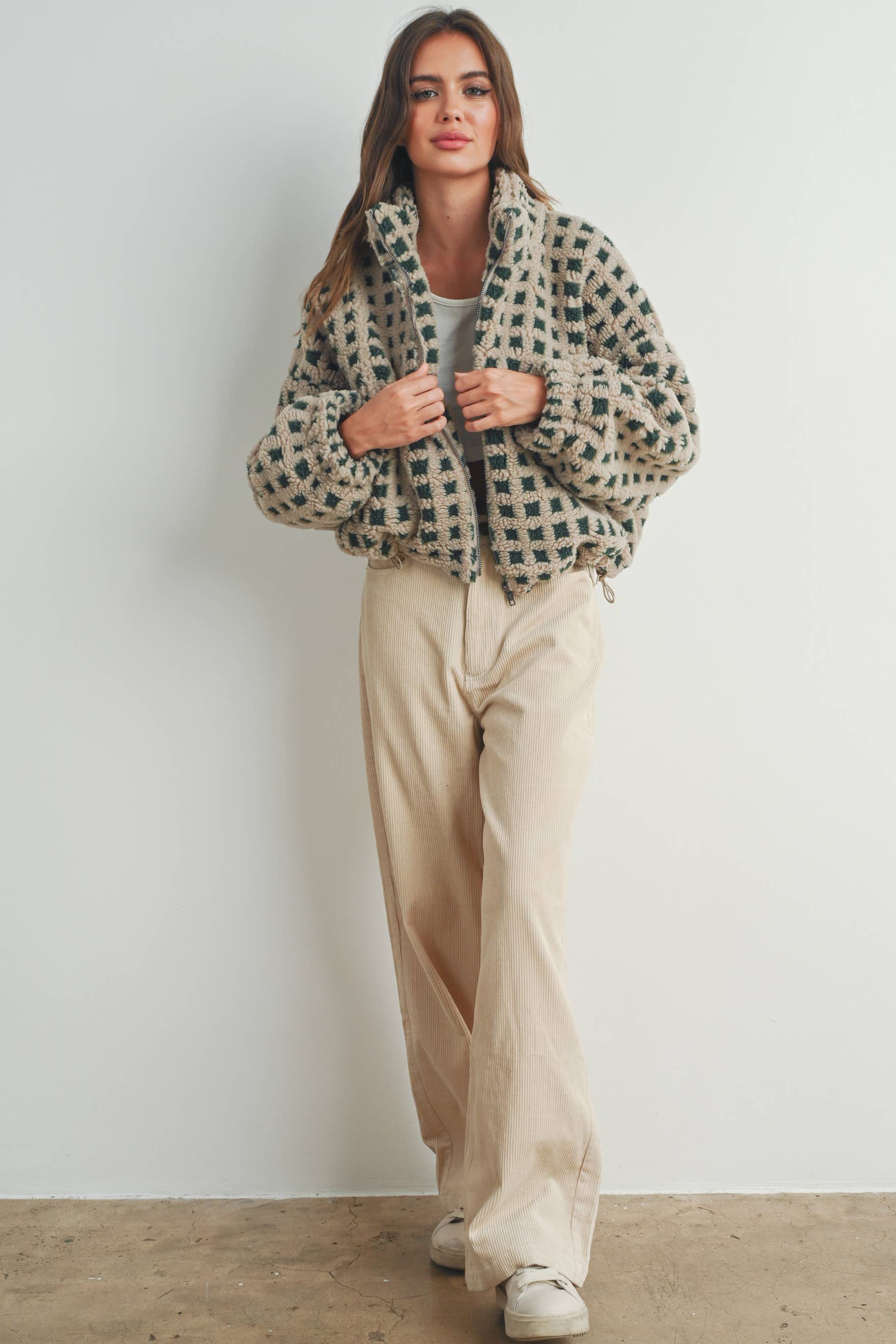 Woman wearing a beige and green checkered fleece jacket with a zip closure, paired with a white crop top and beige corduroy pants.