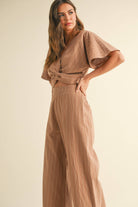 Woman wearing a two-piece striped set with a twist-front crop top and wide-leg pants in cream and tan color options.