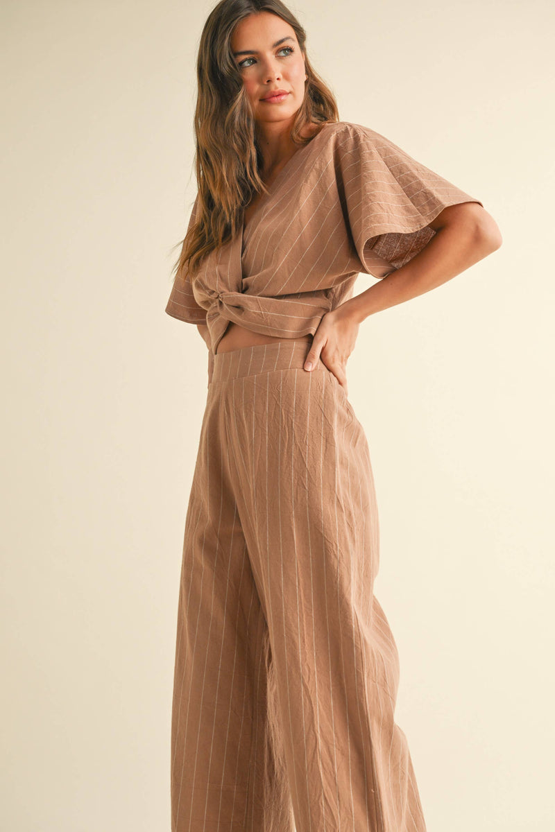 Woman wearing a two-piece striped set with a twist-front crop top and wide-leg pants in cream and tan color options.