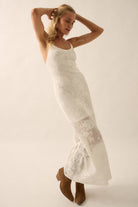 Woman wearing a sheer white lace maxi dress with spaghetti straps and floral detailing.