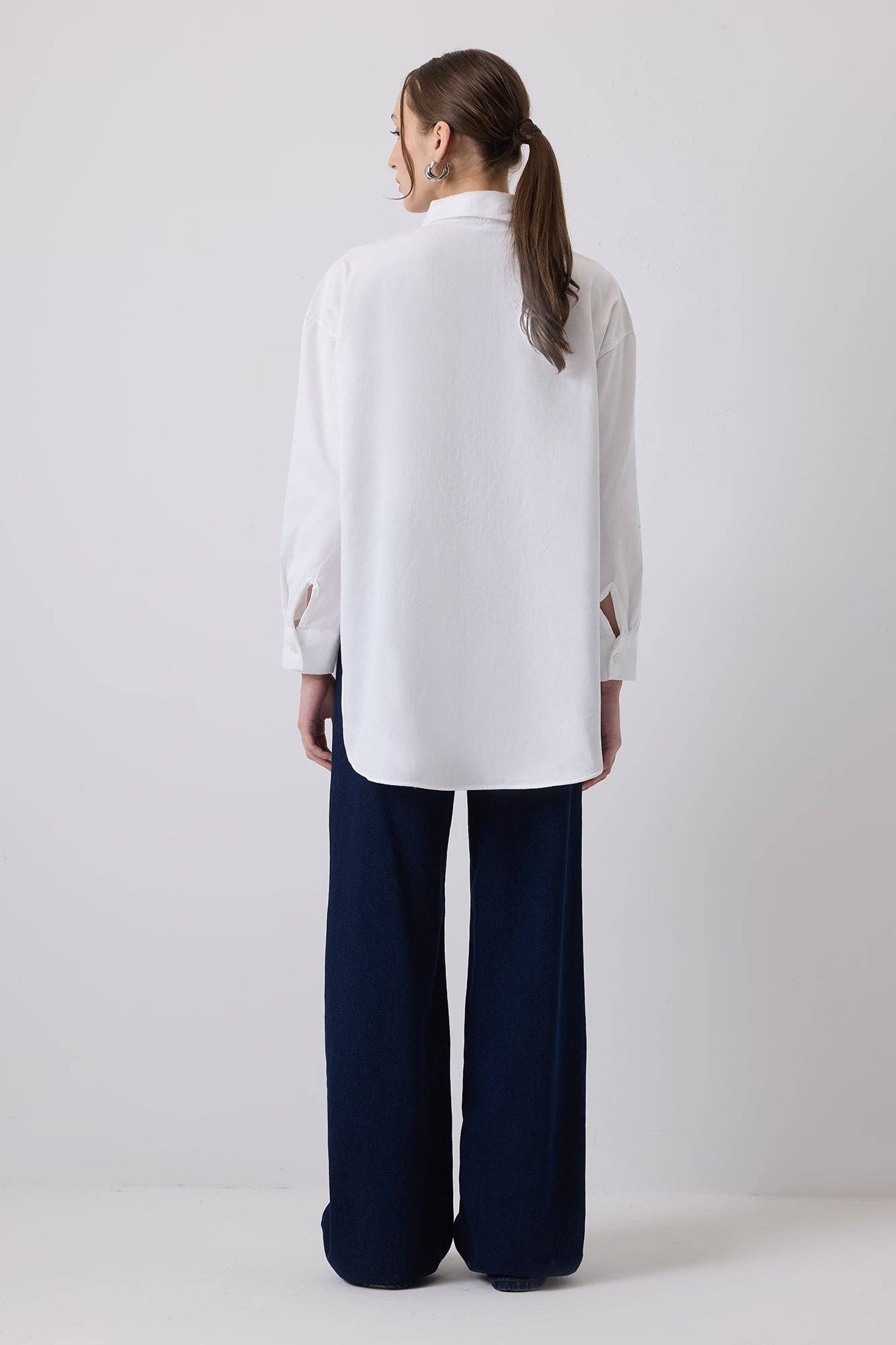 Woman wearing a white oversized shirt with bold blue embroidery on shoulders