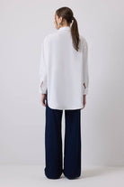 Woman wearing a white oversized shirt with bold blue embroidery on shoulders