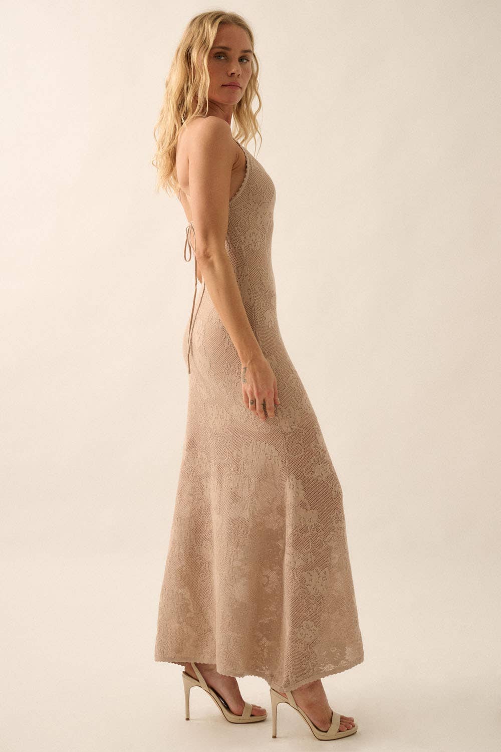 Woman wearing a sheer white lace maxi dress with spaghetti straps and floral detailing.