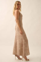 Woman wearing a sheer white lace maxi dress with spaghetti straps and floral detailing.