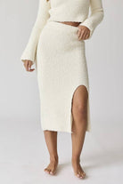 Woman wearing a white round neck long sleeve crop soft knit top and midi skirt set with a side slit.